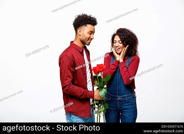 Beautiful elegant couple is hugging and smiling, on gray background. Girl is holding roses