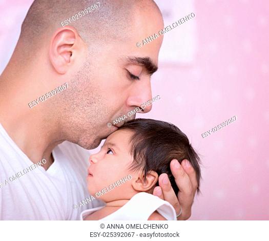 Closeup portrait of a daddy and his baby girl at home, with gentleness kissing his cute newborn daughter, enjoying parenthood