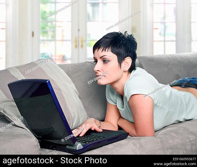 Young women lies on the sofa at home and works on laptop computer
