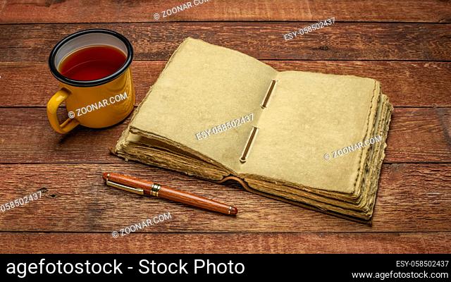 antique leatherbound journal with decked edge handmade paper pages and a stylish pen on a rustic wooden table with a cup of tea, journaling concept