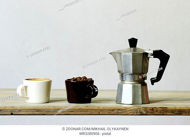 two cups of coffee and beans and percolator on wood