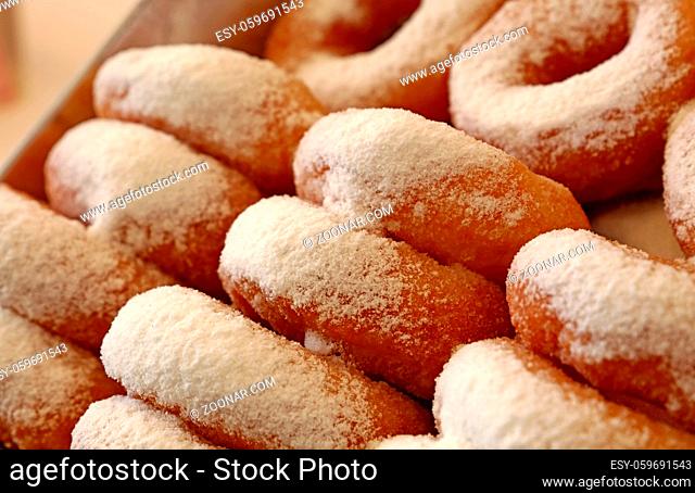 Close up many fresh ring donuts with sugar powder in retail display box, high angle side view