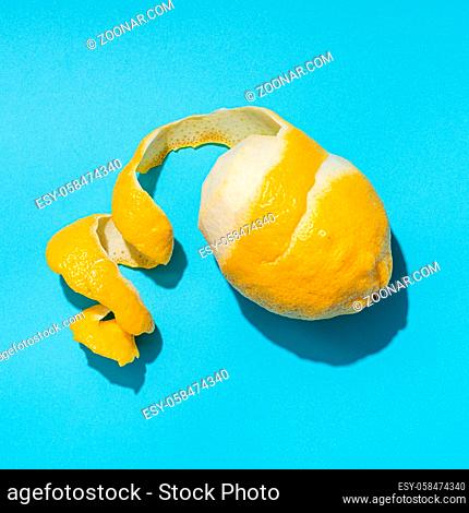 Lemon with spiral peeled zest over blue minimalistic background. Lemon and peel in hard light. Top view or flat lay. Summer minimalistic creative concept and...