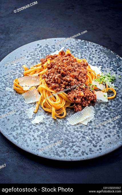 Modern style traditional Italian ragu alla bolognese sauce with linguine pasta noodles and parmesan cheese served as close-up in a ceramic design bowl with copy...