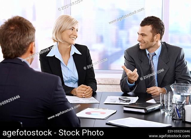 Smiling professionals sitting and talking in meeting room in skyscraper office