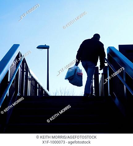 rear view of a man walking alone carrying plastic bags full of shopping, UK