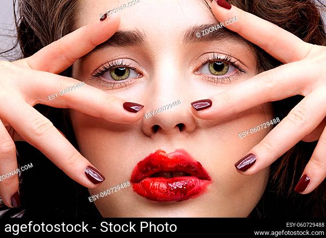 Beauty portrait of young woman with hands on face. Brunette girl with unusual alyapy red female face makeup