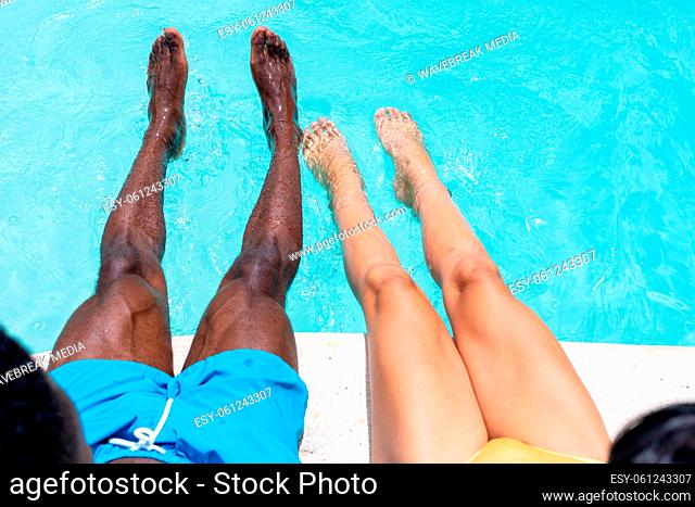 Low section of multiracial young couple dangling legs in swimming pool