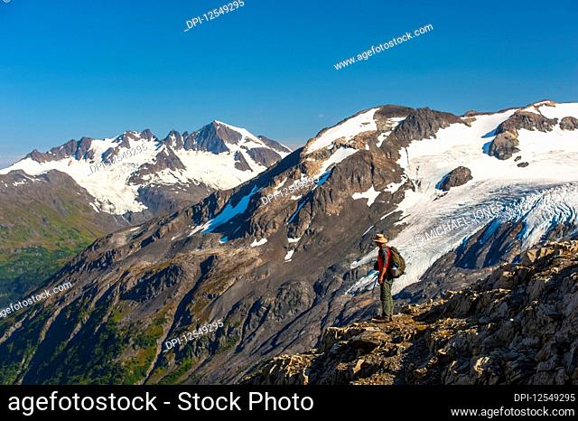 A man hiking near the Harding Icefield Trail with the Kenai Mountains and an unnamed hanging glacier in the background, Kenai Fjords National Park