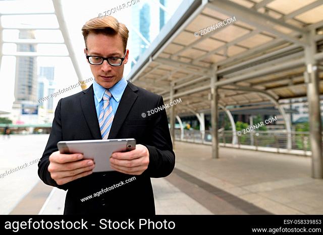 Portrait of young handsome blond businessman in suit at skywalk bridge in the city outdoors