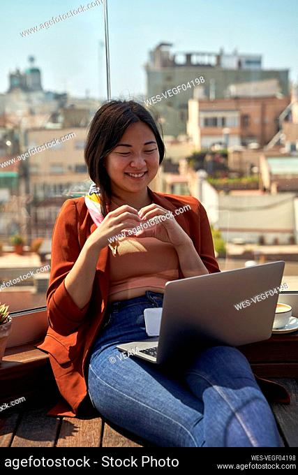 Woman gesturing while smiling at video call on laptop at roof terrace