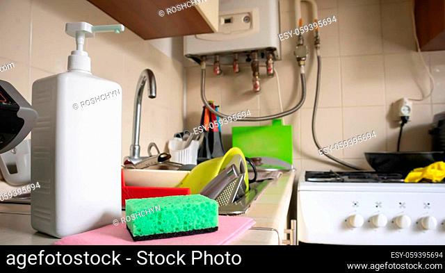 Green sponge and liquid soap dispenser for washing dishes on a dirty sink completely with dishes and kitchen utensils. Washing dishes in the kitchen by hand...