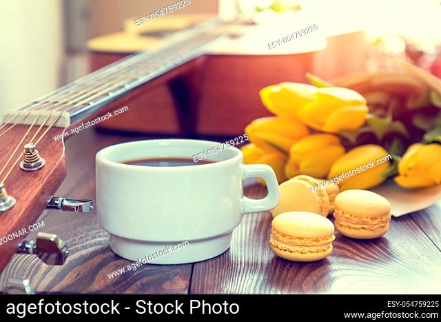 Beautiful spring music background. Cup of coffww, guitar, yellow tulips, musical page on a dark wooden background. Shallow depth of field