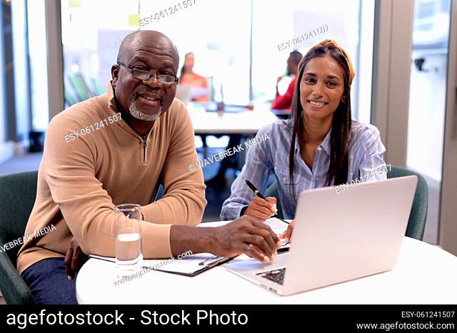 Portrait of multiracial business colleagues with laptop sitting in boardroom during meeting