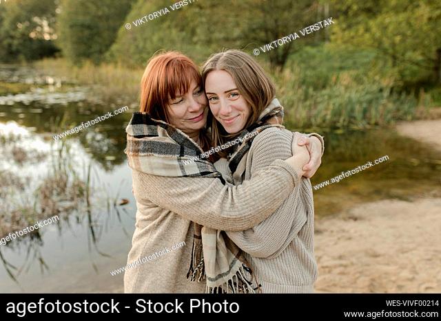 Mother embracing daughter wearing sweater near lake