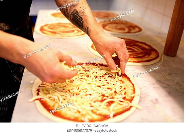 food cooking, culinary and people concept - cook or baker hands adding grated cheese to pizza at pizzeria