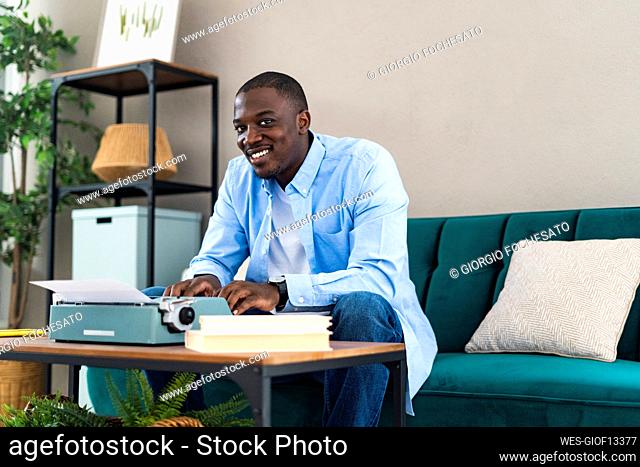 Smiling man with typewriter on table at home