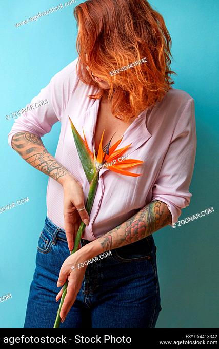 Red-haired girl with a tattoo holds an exotic strelitzia flower on a blue background. Mothers Day