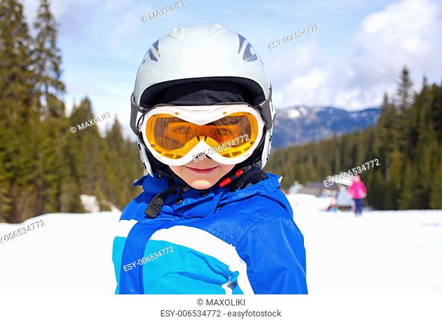 Portrait of little boy in helmet and ski goggles on a sunny day in the mountains. Active outdoor childhood concept