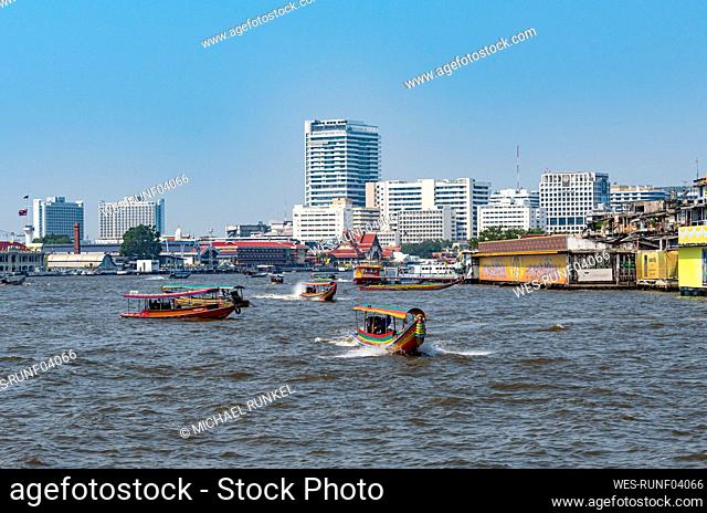Thailand, Bangkok, Ferries on Chao Phraya river with city skyline in background