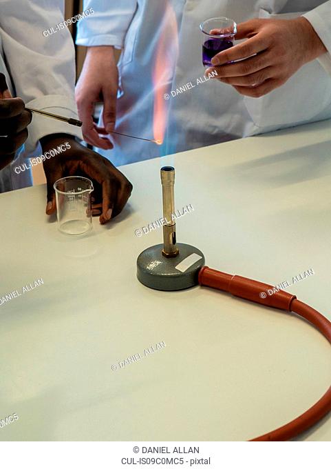 Young female and male scientists experimenting with liquid and bunsen burner in laboratory, cropped