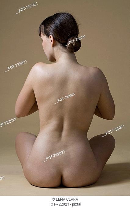 Rear view of a nude woman sitting crossed-legged
