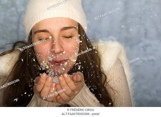 Young woman wearing winter clothing, blowing handful of confetti