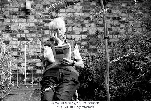 Old man reading the newspaper in a backyard