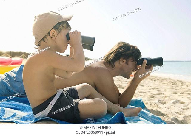 Father and son looking through binoculars on beach