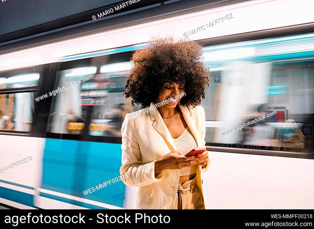 Smiling woman using smart phone in front of moving subway train