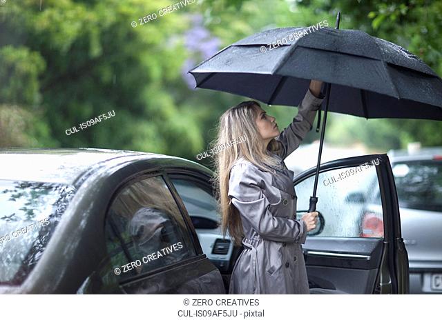 Young woman struggling to put up umbrella