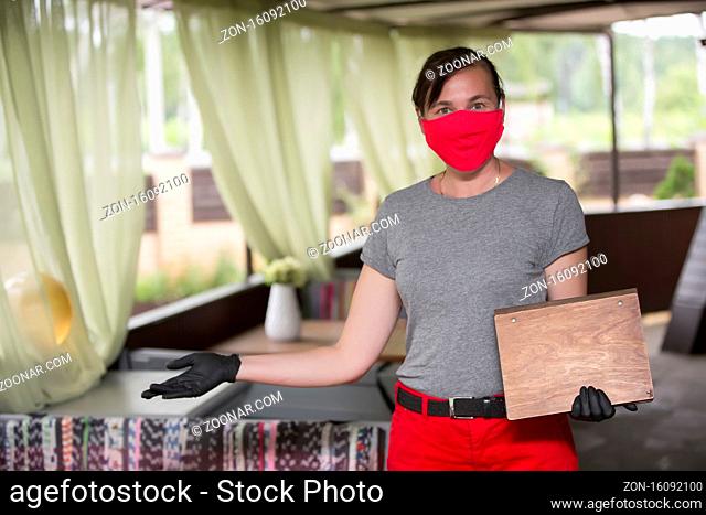 Happy waiter with protective mask holds the menu and invites to the restaurant