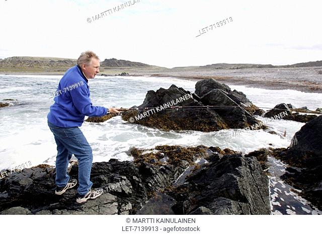 A man is fishing on the rocks by the Arctic Ocean in Vardö in the Varanger Peninsula, Norway. Vuoreija Vuorea Vardo Vardo