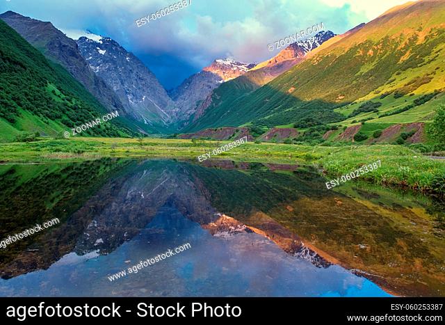 Beautiful landscape with high mountains with illuminated peaks, reflection in lake, sunlight of sunrise