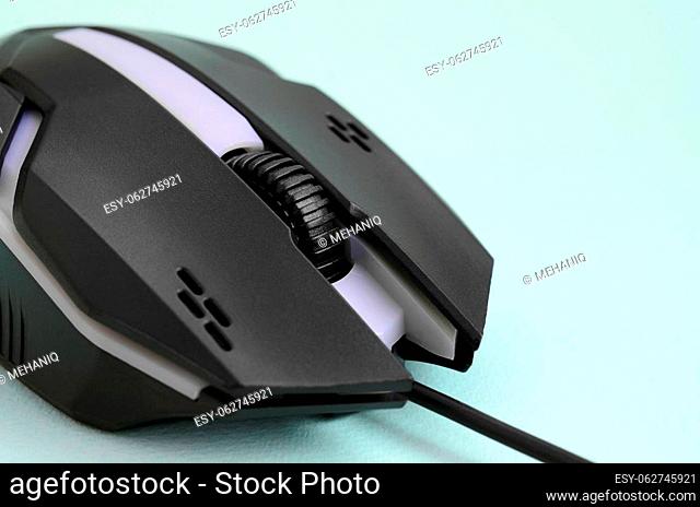 Closeup of a black gaming optical mouse on a blue background. Device for cybersport and online video games