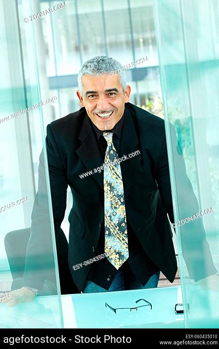 Nature businessman standing leaning to desk in modern glass office, smiling