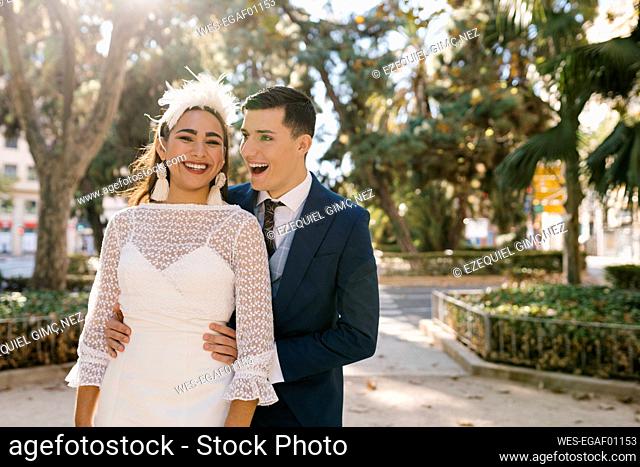 Smiling groom embracing bride while standing in park