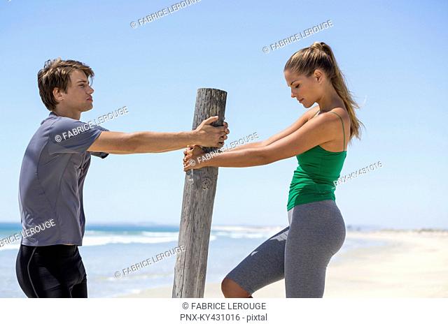 Man assisting a woman to exercise on the beach