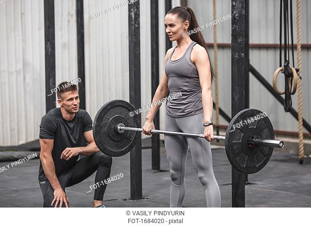 Male instructor looking at young woman crossfit training at gym