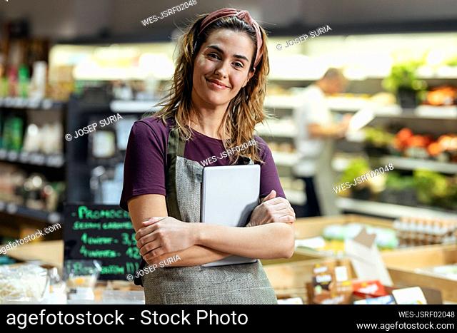 Smiling store owner standing with tablet PC at organic market