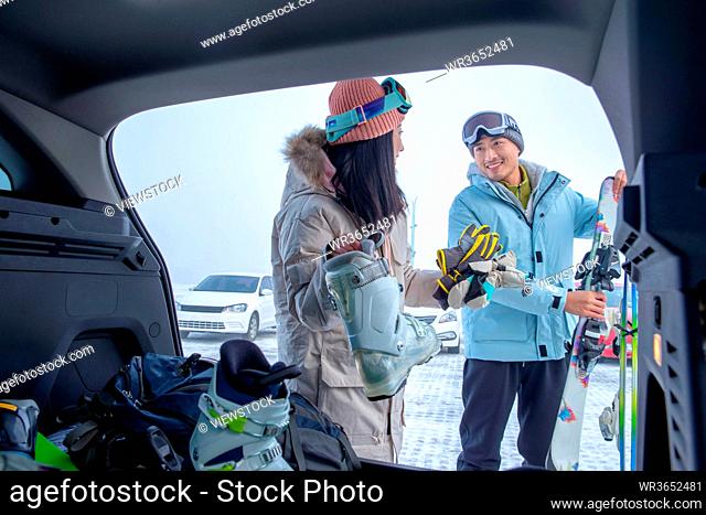 Parking lot young couples out of the car trunk ski equipment