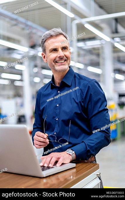 Smiling businessman with laptop in factory
