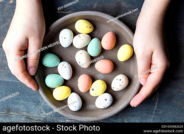 Hands holding stylish pastel painted easter eggs in ceramic grey plate on vintage old wooden background, Happy Easter concept