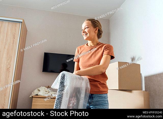 Smiling woman removing bubble wrap from picture frame at home