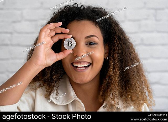 Smiling woman covering eye with silver cryptocurrency