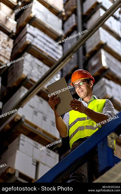 Smiling worker wearing eyeglasses using tablet PC working in warehouse