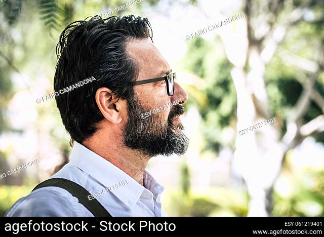 Side portrait of caucasian adult mature man with beard and eyewear looking in front with park nature geen defocused background