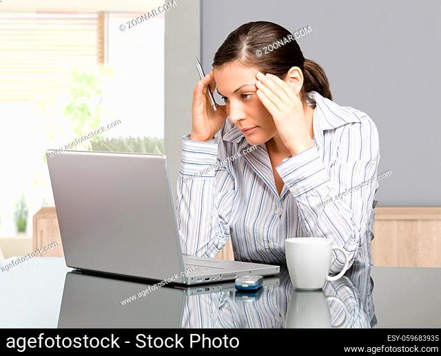 Young woman sitting at desk working with laptop computer at home, serious, thinking