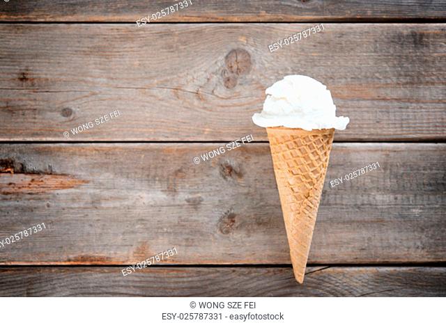 Single vanilla ice cream in a waffle cones over wooden background with copy space