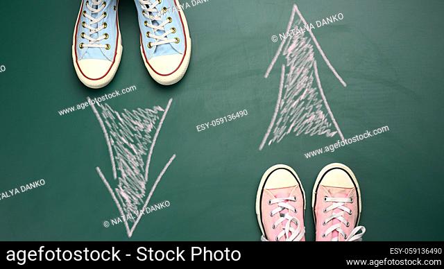 two pairs of textile sneakers stand opposite each other on a green background. The concept of mismatch of direction of movement, difference of thinking
